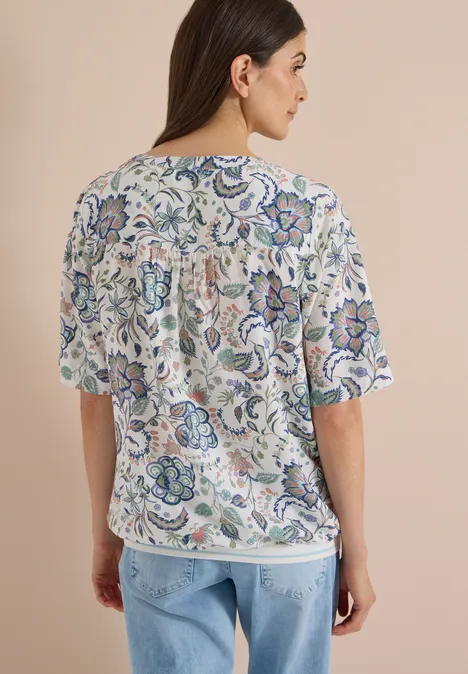 Frau von hinten in hellem T-Shirt mit farbenfrohem Blumenmuster.