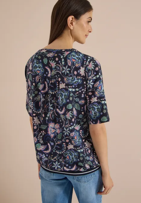 Rückansicht einer Frau in geblümter Bluse und Jeans.