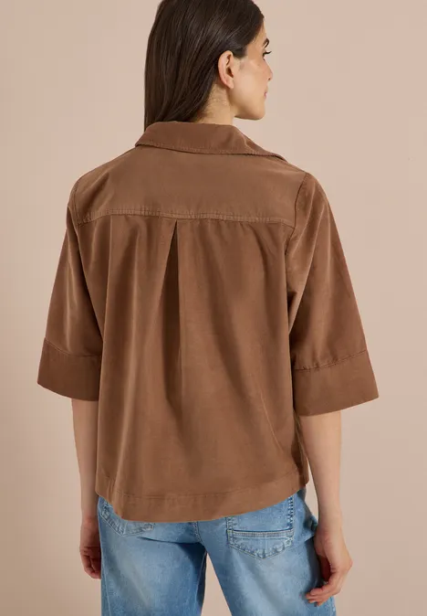 Chemisier à manches courtes uni creamy mocha Frau von hinten in lockerer brauner Cord-Hemdbluse mit 3/4-Ärmeln und blauen Jeans vor beigem Hintergrund.