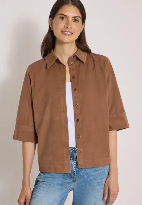 Chemisier à manches courtes uni creamy mocha Frau trägt kastiges braunes Leinenhemd, weißes Top und blaue Jeans, lächelt