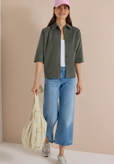 Chemisier à manches courtes uni dried olive green Frau in weitem Jeans-Culotte, olivgrünem Hemd, weißem Top, Sneakern und pinker Kappe trägt Tasche.
