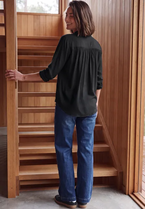 Frau in schwarzer Bluse und Jeans geht eine Holztreppe in einem hellen Holzhaus hinauf.