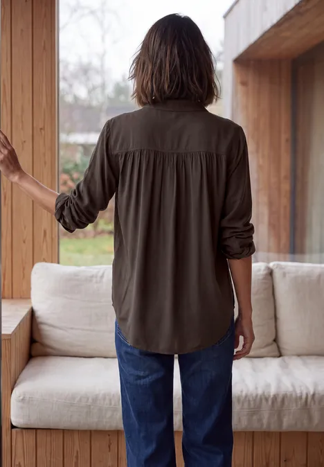 Langarm Hemdbluse mit Knopfleiste truffle brown Person mit schulterlangem braunen Haar in olivgrünem Hemd und Jeans steht in hölzernem Raum am Fenster.
