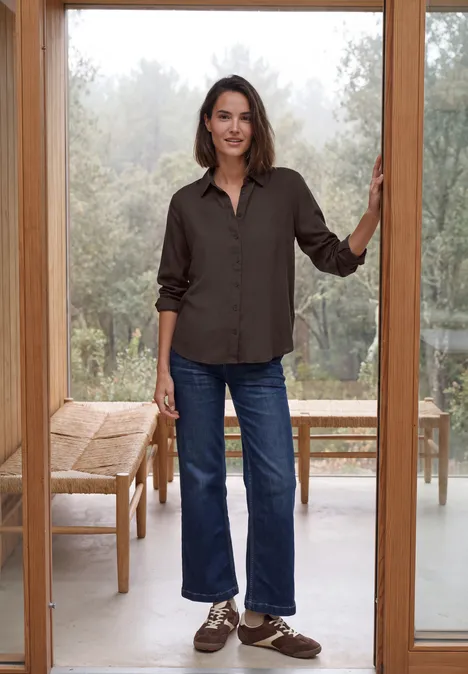 Langarm Hemdbluse mit Knopfleiste truffle brown Eine Frau steht lässig in einer Türöffnung, trägt braunes Hemd, gerade geschnittene Jeans und braune Schuhe.