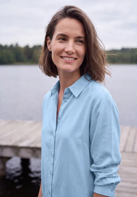 Langarm Hemdbluse mit Knopfleiste cosmopolitan blue Eine lächelnde Frau in hellblauem Hemd steht auf einem Steg vor einem ruhigen See.