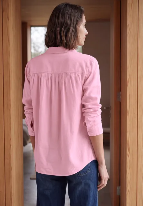 Achteraanzicht van iemand in roze blouse en spijkerbroek, staand in een houten deuromlijsting.