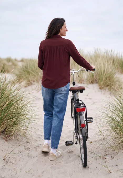 Chemisier à manches longues avec patte de boutonnage red wine Une personne pousse son vélo à travers des dunes sablonneuses et des herbes de plage sous un ciel nuageux.