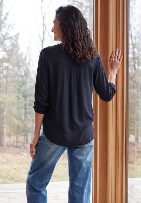 Frau in Jeans und schwarzem Oberteil blickt mit dem Rücken zur Kamera aus einem Fenster.