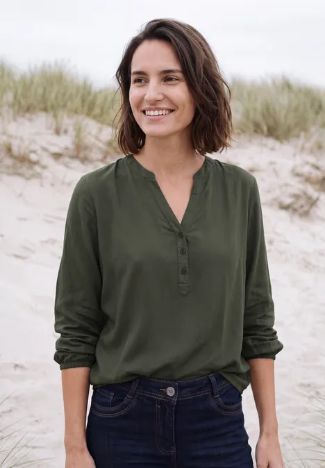 Frau am Strand mit grüner Bluse, lächelnd vor Dünenkulisse