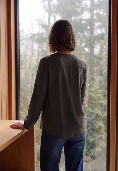 Eine Person steht am Fenster und schaut auf einen nebligen Wald.