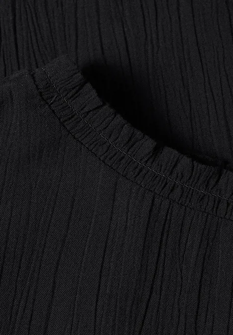 Blouse à manches longues et col rond avec détails smockés Black Gros plan sur un tissu noir plissé avec bord élastique.