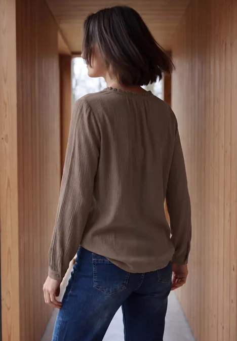 Frau von hinten in Holzflur, trägt braunes Langarmshirt und blaue Jeans.