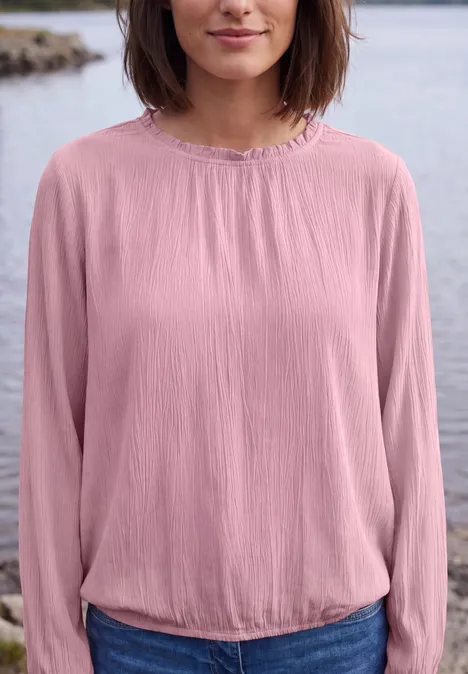 Vrouw in roze blouse bij een meer, torso zichtbaar van kin tot taille