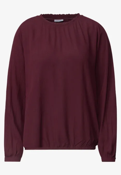 Dunkelrote Bluse mit langen Ärmeln und rundem Halsausschnitt.