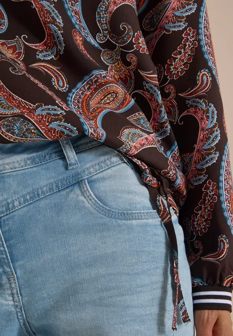 Helle Jeans und eine braune Bluse mit Paisleymuster, seitlich geknotet.