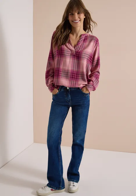 Langarm Tunika mit Karomuster velvet rose Frau in pinkkarierter Bluse und ausgestellten Jeans posiert lässig mit Händen in den Taschen und lächelt.