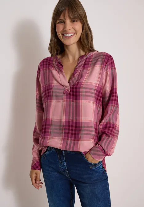 Langarm Tunika mit Karomuster velvet rose Frau in locker sitzender karierter roter Bluse und Jeans lächelt in die Kamera.