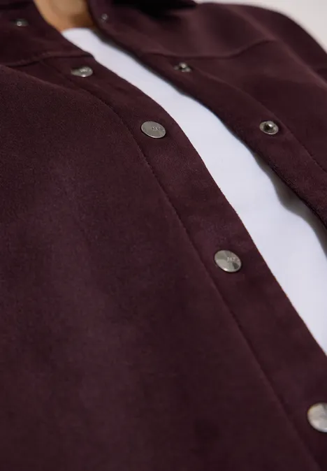 Nahaufnahme einer dunkelroten Jacke mit silbernen Druckknöpfen über weißem Shirt.