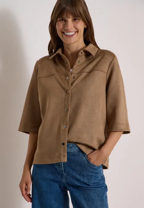 Velours Hemdbluse mit Tapedetails creamy mocha Frau in lässigem braunem Hemd mit 3/4-Ärmeln und Jeans, die lächelnd in die Kamera schaut.