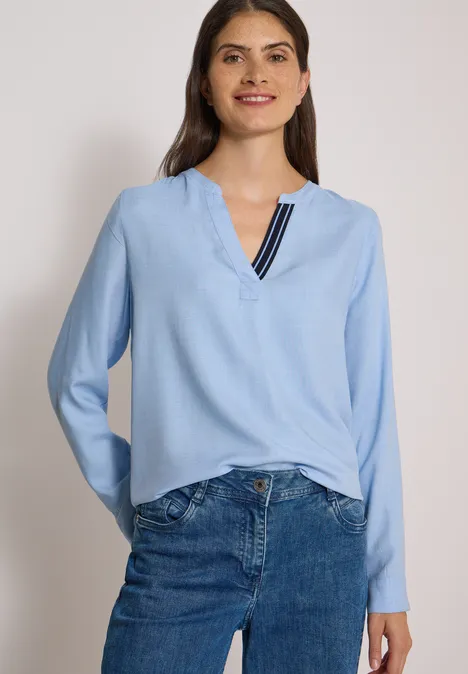 Langarm Tunika mit Split Neck und Tape blouse blue melange Eine Frau trägt eine hellblaue Bluse mit V-Ausschnitt und Streifendetail zu blauen Jeans.