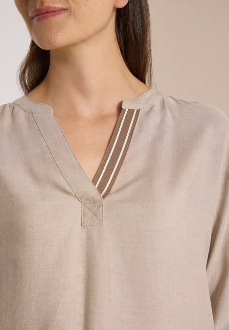 Nahaufnahme von beige Bluse mit V-Ausschnitt und drei weißen Zierstreifen am Halsausschnitt