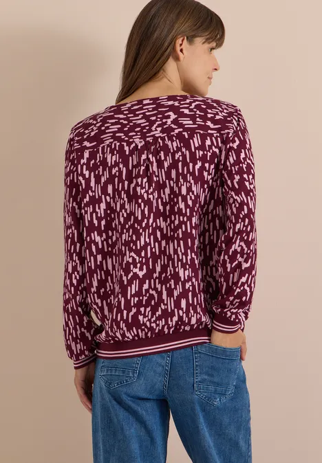 Vrouw van achteren in een paarse, abstract gemêleerde trui en jeans