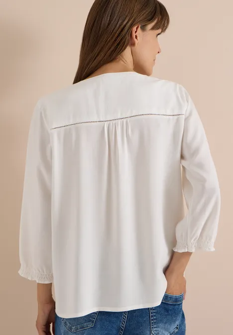 Frau in weißer Bluse mit Dreiviertelärmeln, Rückenansicht, trägt Jeans.