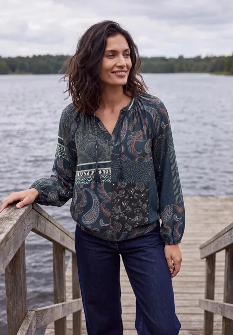 Langarm Tunika mit Bändern und Print urban dark blue Frau in gemusterter Bluse und Jeans auf hölzernem Steg am See, lächelnd.
