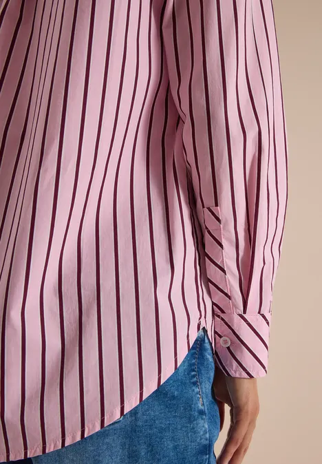 Seitlich sieht man eine Person in einem rosa Hemd mit schwarzen Streifen und blauen Jeans