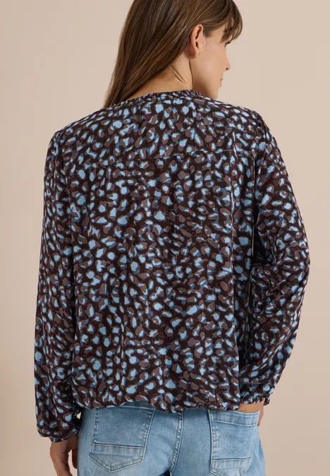 Frau von hinten trägt eine dunkelbraune Bluse mit hellblauem Leopardenmuster und eine helle Jeans.