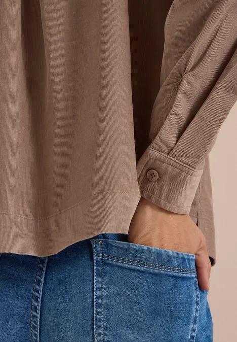 Nahaufnahme einer Person mit Hand in der Jeans-Tasche, darüber ein beige-braunes Hemd.