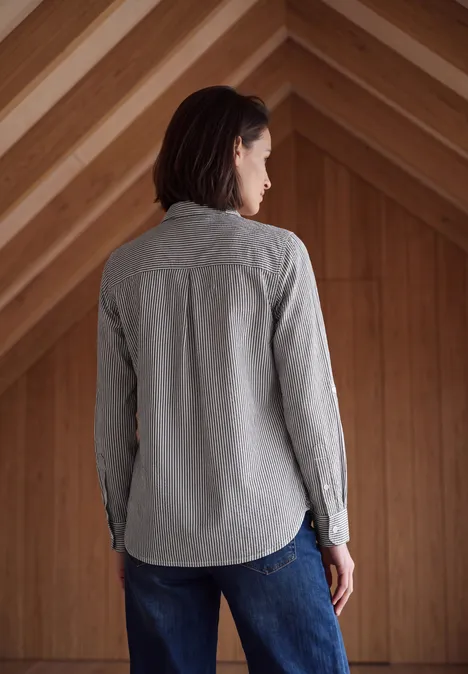 Seersucker Hemdbluse mit Streifen truffle brown Frau steht von hinten in grauem Hemd und Jeans in einem holzverkleideten Raum.