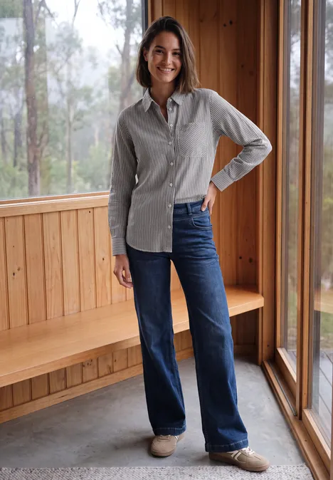Seersucker Hemdbluse mit Streifen truffle brown Frau im hellen Holzzimmer, lächelt, trägt graues Hemd, blaue Jeans und helle Schuhe.