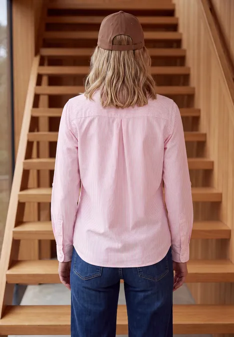 Overhemd met lange mouwen en strepen mellow rose Iemand van achteren in roze blouse, spijkerbroek en bruine muts voor een houten trap.