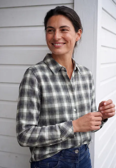 Flanellen blouse met lange mouwen en ruitjespatroon vanilla white Vrouw in geruit overhemd staat bij een witte houten gevel en glimlacht opzij.