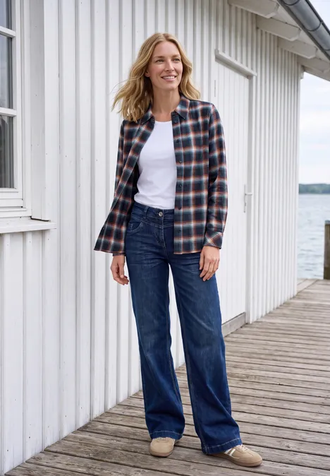 Flanellen blouse met lange mouwen en ruitjespatroon urban dark blue Vrouw in geruit overhemd en spijkerbroek staat op een steiger voor een wit houten huis aan het water.