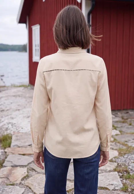 Langarm Hemdbluse aus Cord in Unifarbe cashmere beige Eine Person in hellbeiger Jacke und Jeans steht mit dem Rücken zum Betrachter vor einem roten Haus am Wasser.