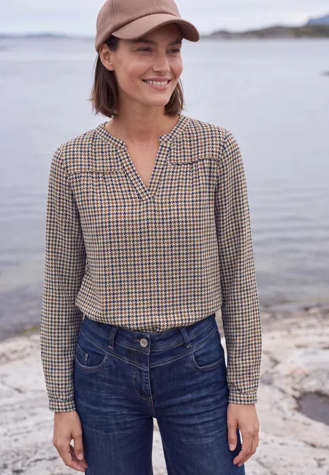 Tuniek met lange mouwen, split in de hals en print mocha brown Vrouw lacht in geruit hemd, jeans en pet aan de waterkant.