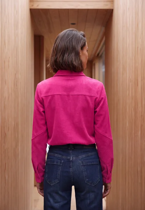 Langarm Hemdbluse aus Cord in Unifarbe pink flash Frau steht mit Rücken zur Kamera, trägt pinke Bluse und blaue Jeans in einem hölzernen Flur.