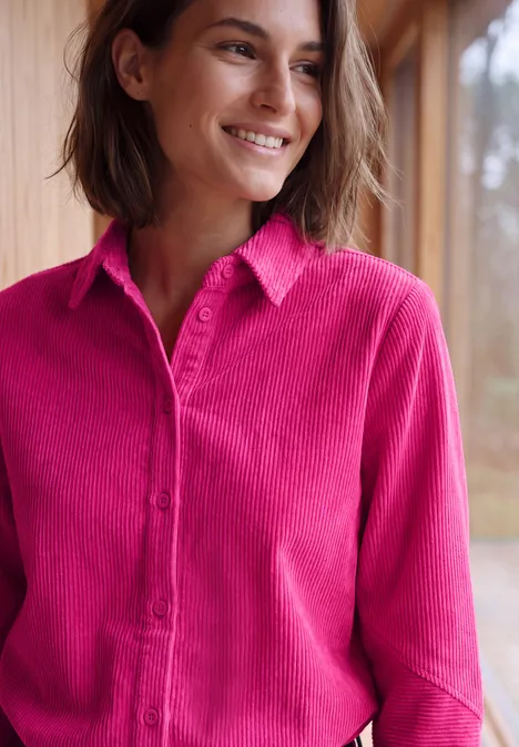 Langarm Hemdbluse aus Cord in Unifarbe pink flash Junge Frau mit kinnlanger brauner Frisur lächelt und trägt eine pinke Bluse vor hellem Holzhintergrund.