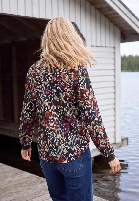 Chemisier à manches longues, à col fendu et imprimé truffle brown Eine Frau mit blondem Haar, buntem Hemd und Jeans läuft auf einem Steg am See.