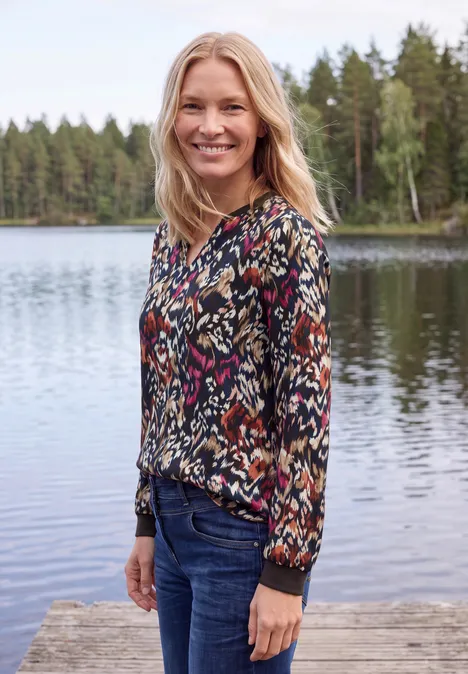 Chemisier à manches longues, à col fendu et imprimé truffle brown Lächelnde Frau in gemusterter Bluse und Jeans steht auf einem Steg vor See und Wald.