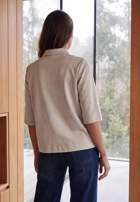 Kurzarm Hemdbluse in Unifarbe cashmere beige Frau steht mit dem Rücken zur Kamera, trägt helle 3/4-Arm-Bluse und blaue Jeans in modernem Raum.