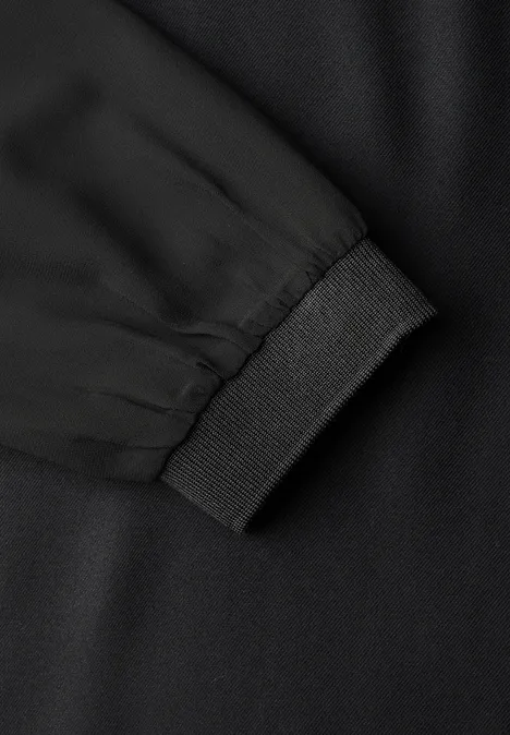 Langarm Bluse mit V-Neck und Strukturmix Black Nahaufnahme einer schwarzen Jacken-/Pullover-Ärmel mit elastischem Bündchen auf schwarzem Stoff.