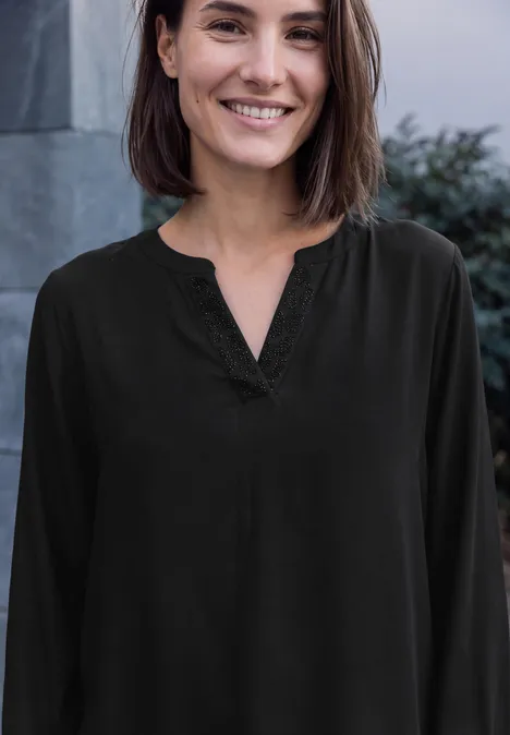 Langarm Tunika mit Split Neck und Detail Black Eine Frau mit braunen schulterlangen Haaren lächelt in schwarzer Bluse vor neutralem Hintergrund.