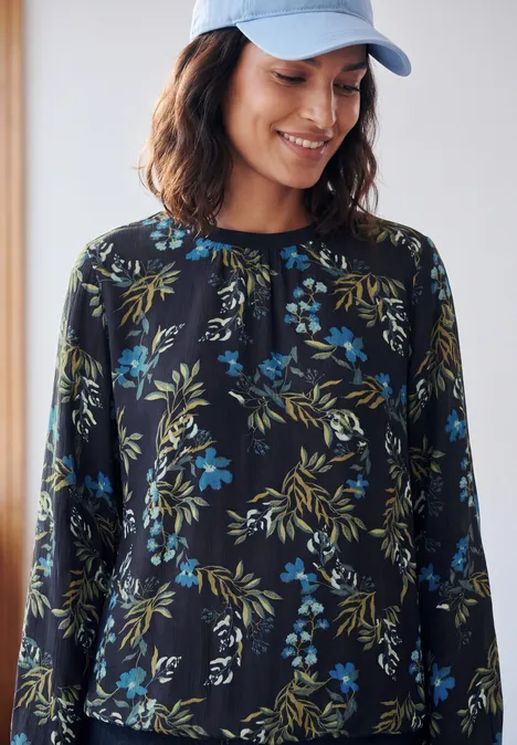 Eine Frau trägt eine blaue Kappe und ein schwarz-blau-grünes Blumenshirt