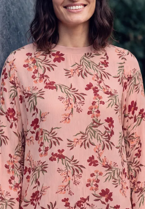 Crepe Bluse mit floralem Muster soft blossom rose Frau trägt ein rosa Langarmshirt mit bunten Blumendrucken und lächelt sanft.