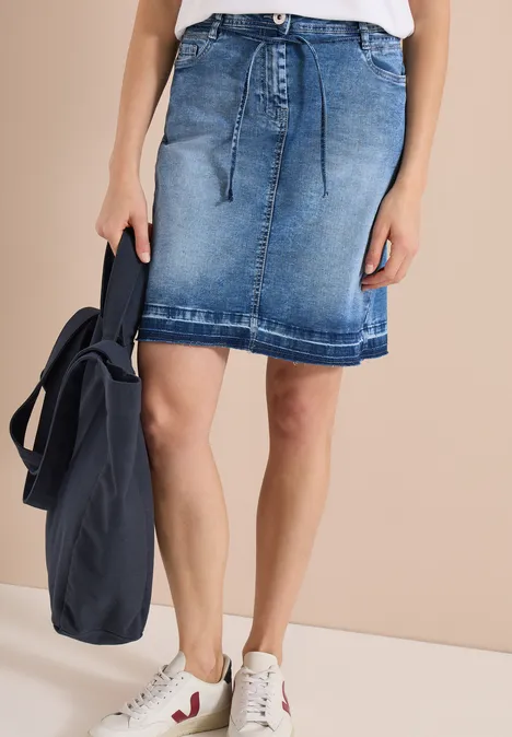 Vrouw met jeansrok, witte sneakers en een donkerblauwe rugzak.