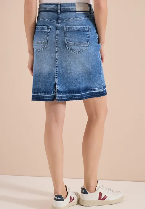 Achteraanzicht van een model in een blauwe denimrok en witte sneakers.