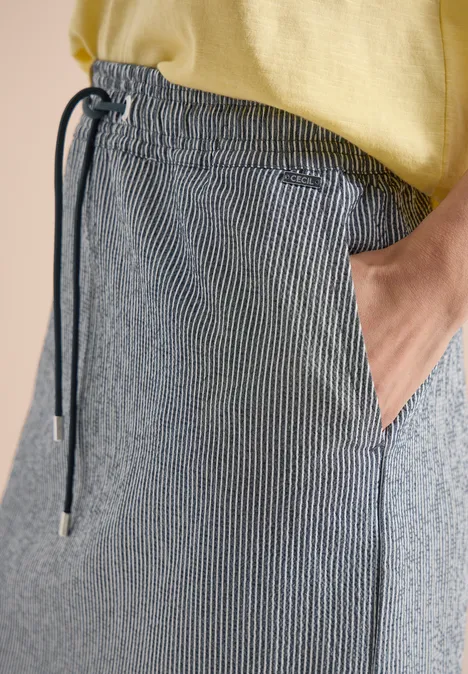 Nahaufnahme einer Person in grauen, gestreiften Jogginghosen mit Kordelzug und gelbem T-Shirt, Hand in Tasche